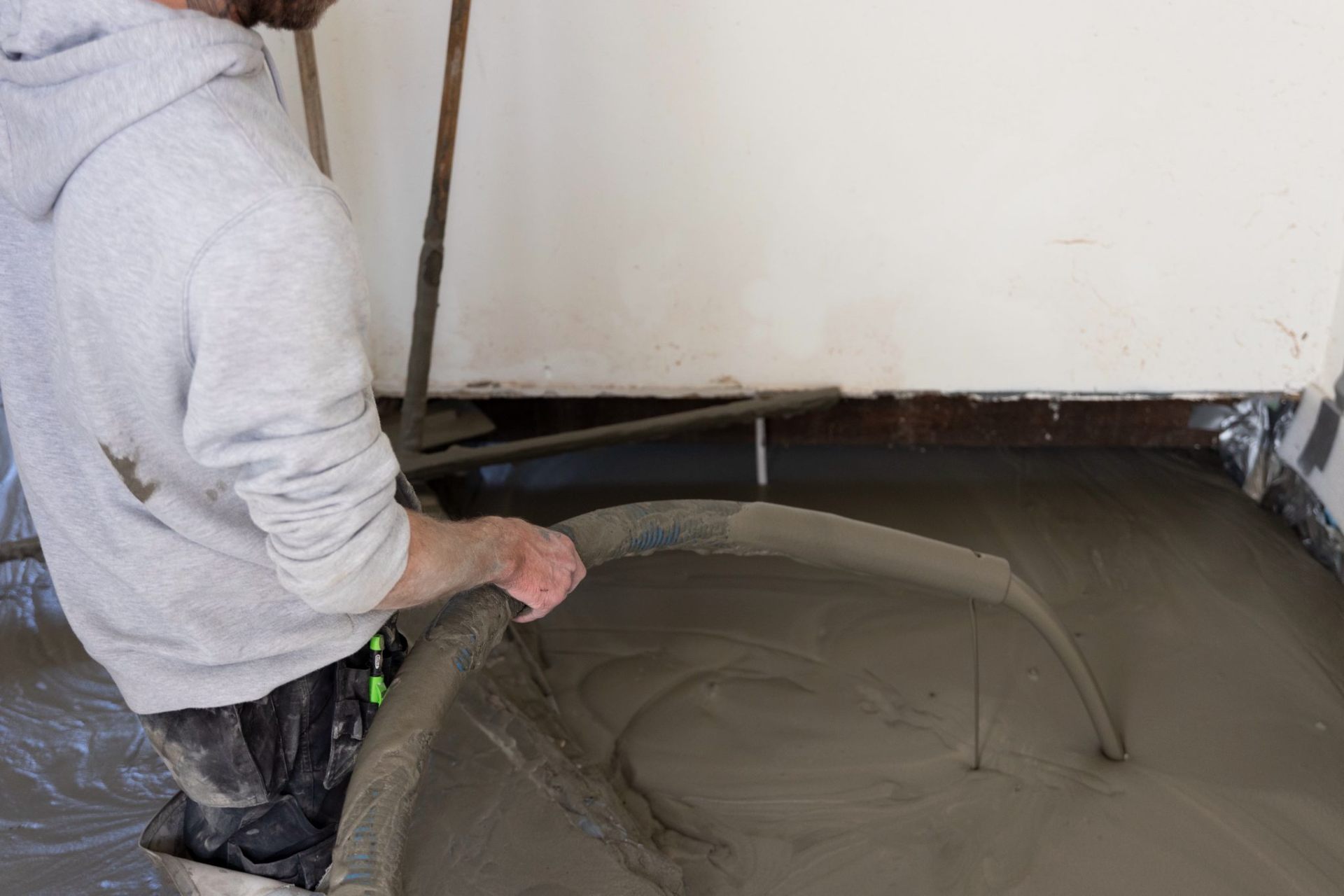 Vakman stort vloeibare Isopact isolatiemortel met slang en pomp op de ruwe ondervloer van een woning