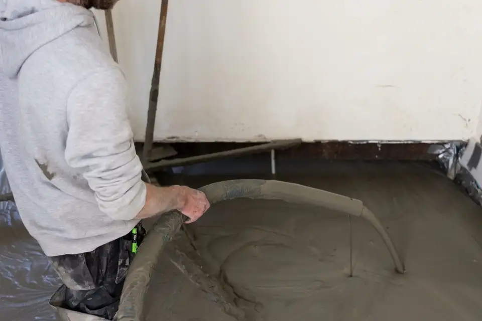 Vakman stort vloeibare Isopact isolatiemortel met slang en pomp op de ruwe ondervloer van een woning