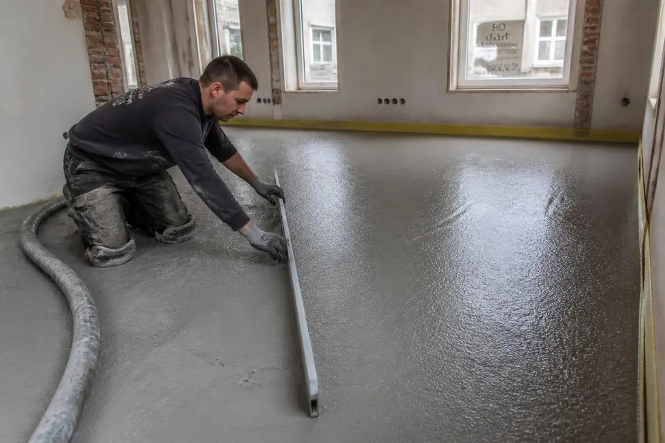 Vloerspecialist vlakt verse schuimbeton af met een rei tijdens een verbouwing