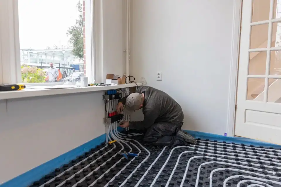 Installateur legt vloerverwarmingsleidingen op een uitgeharde Isopact ondervloer als voorbereiding op de afwerkvloer